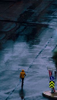一个穿着黄色雨衣的人走过潮湿的道路，天空是灰色的，多云