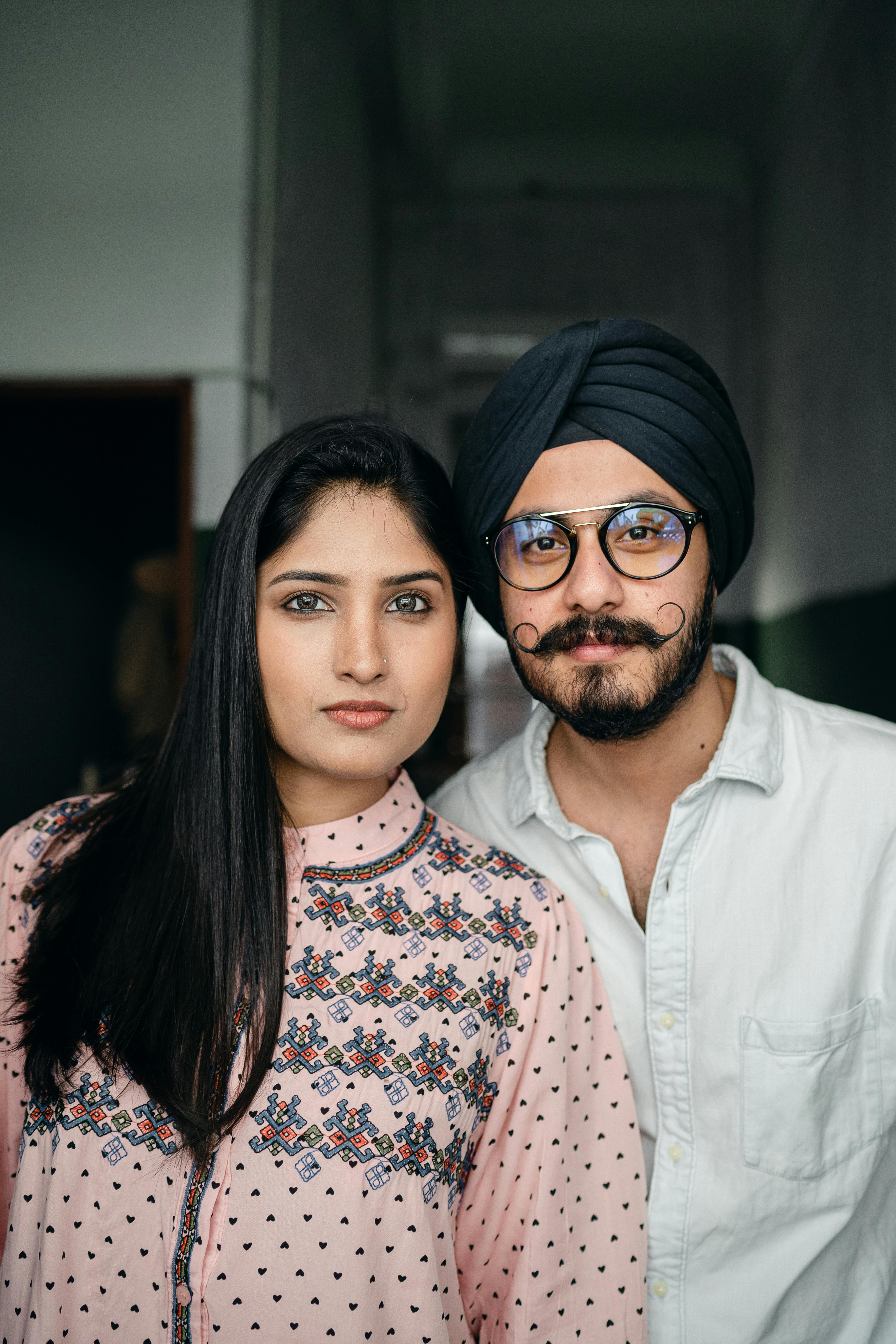 Portrait of positive young Sikh couple in casual outfits wearing turban and eyeglasses standing close to each other and looking at camera
