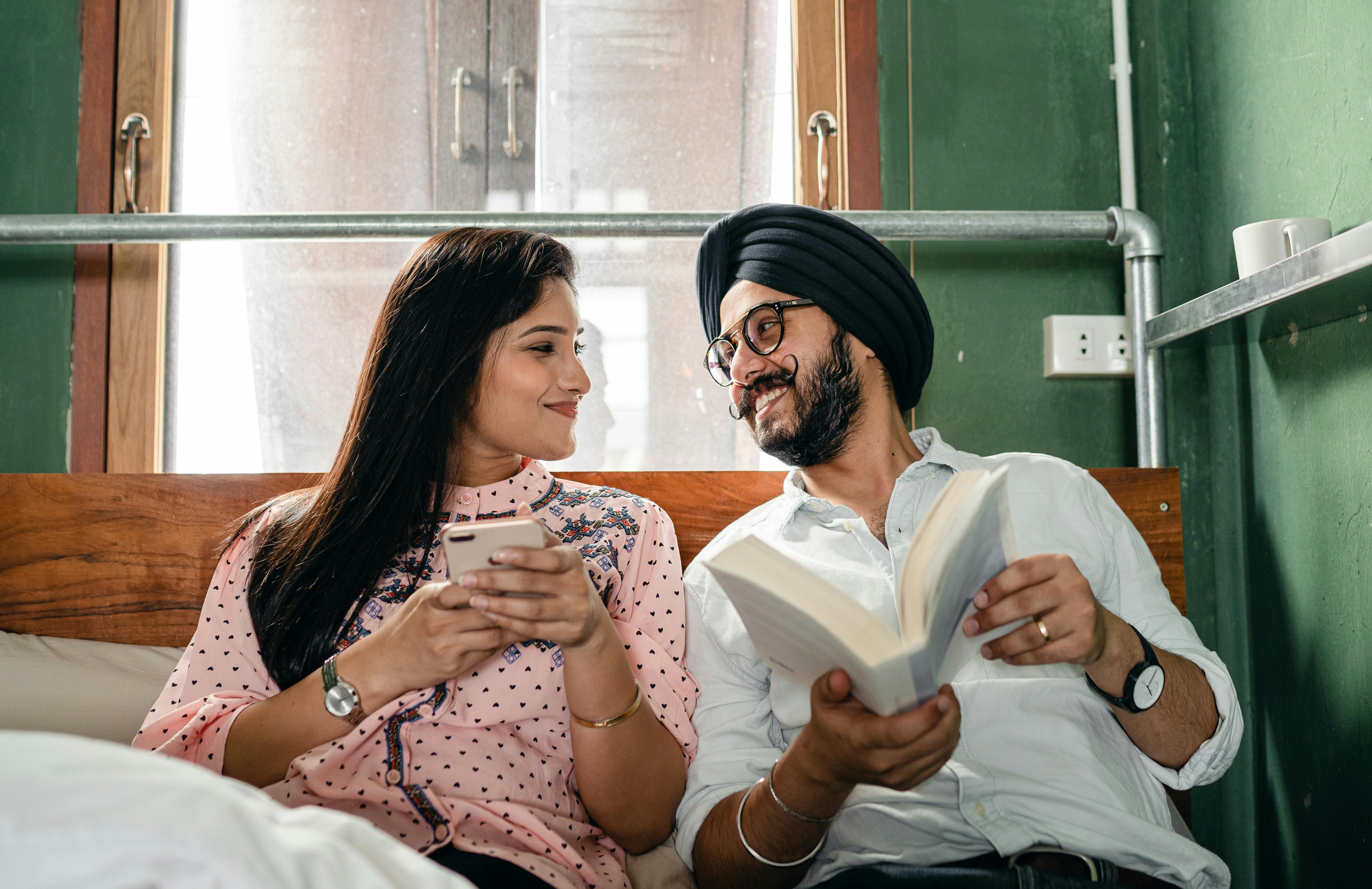 cheerful couple with book and smartphone on bed