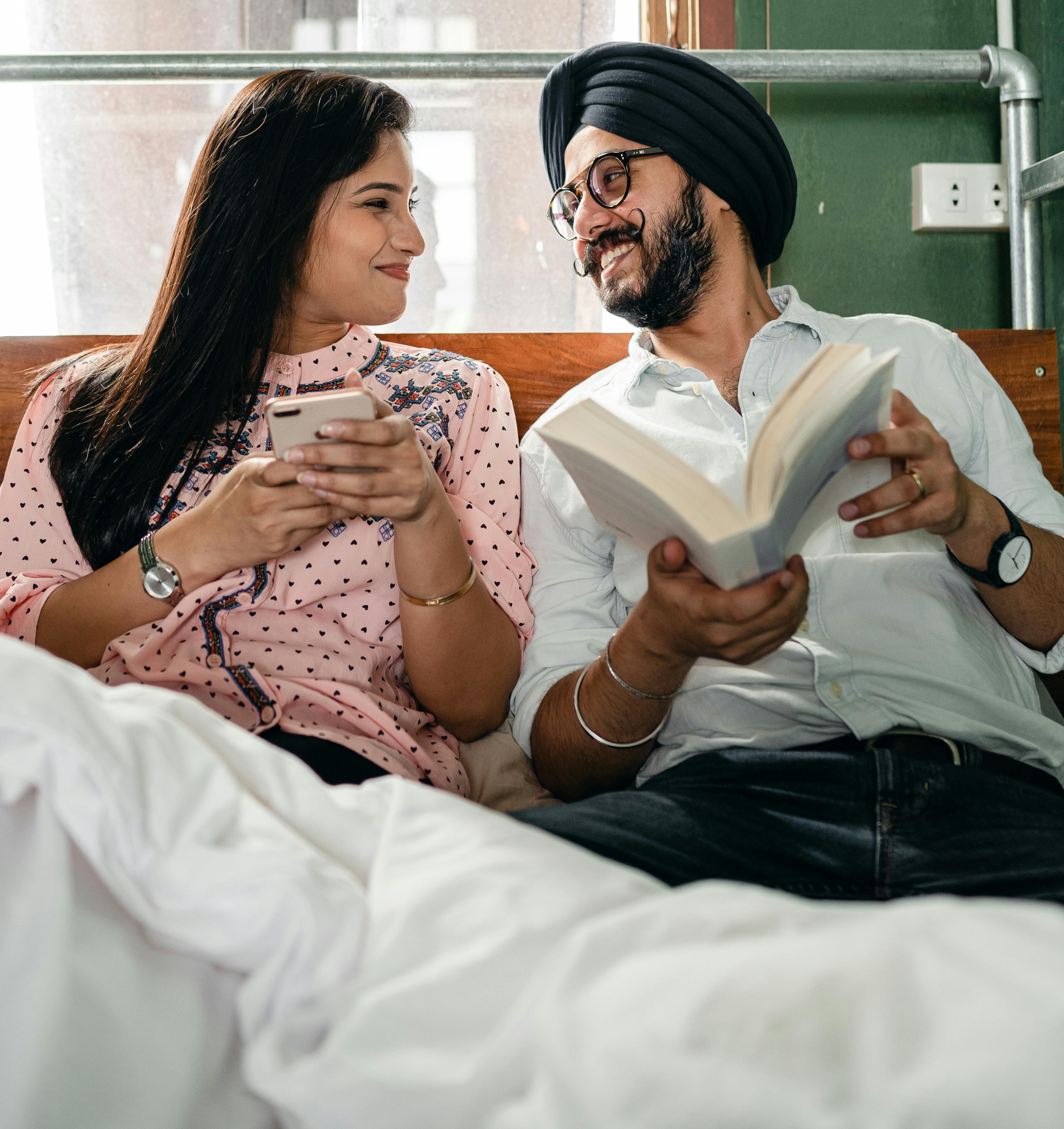 cheerful couple with cellphone and book on bed