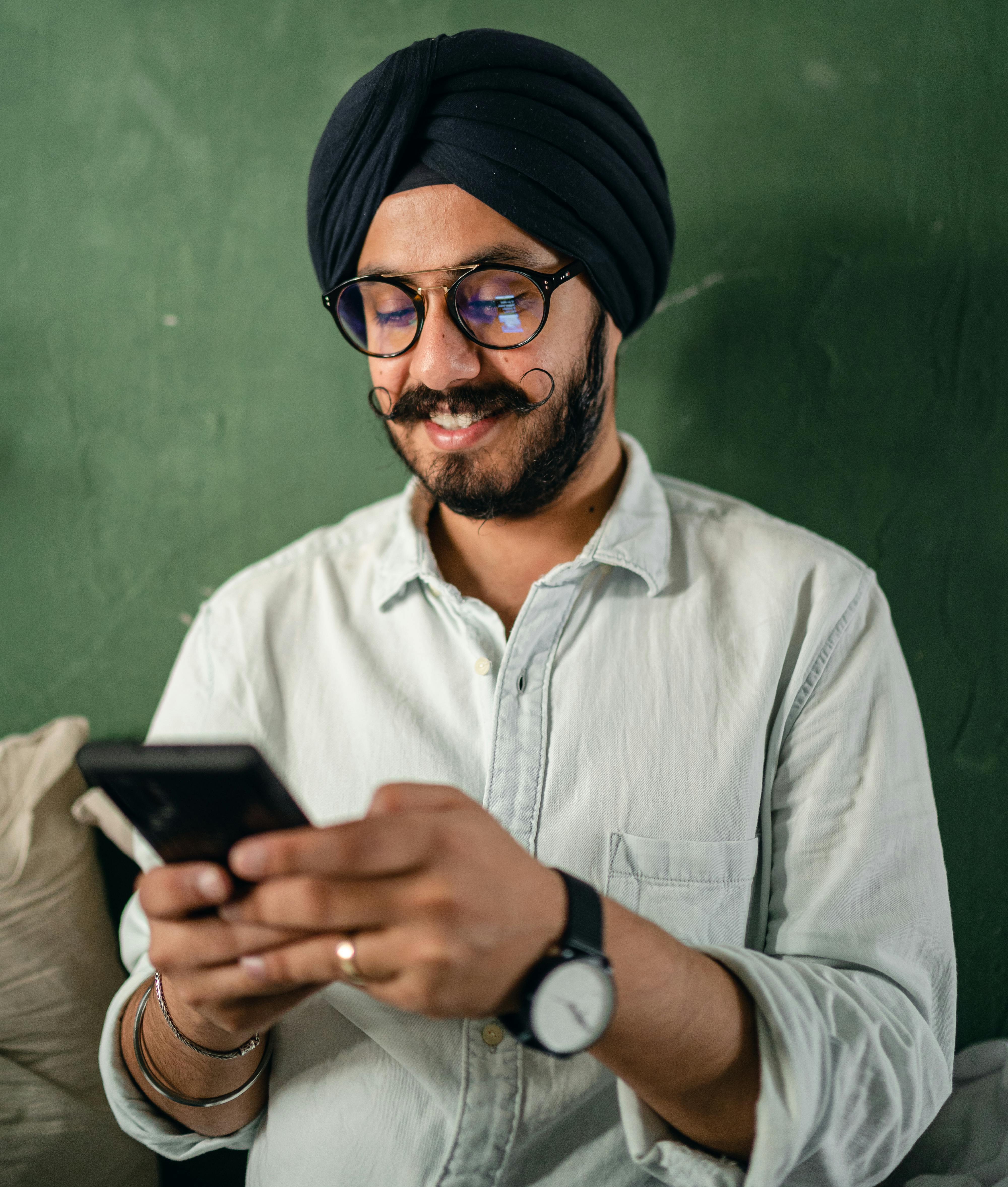 content male in turban and eyeglasses using smartphone