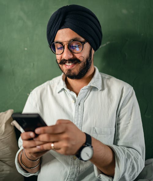 Content male in turban and eyeglasses using smartphone