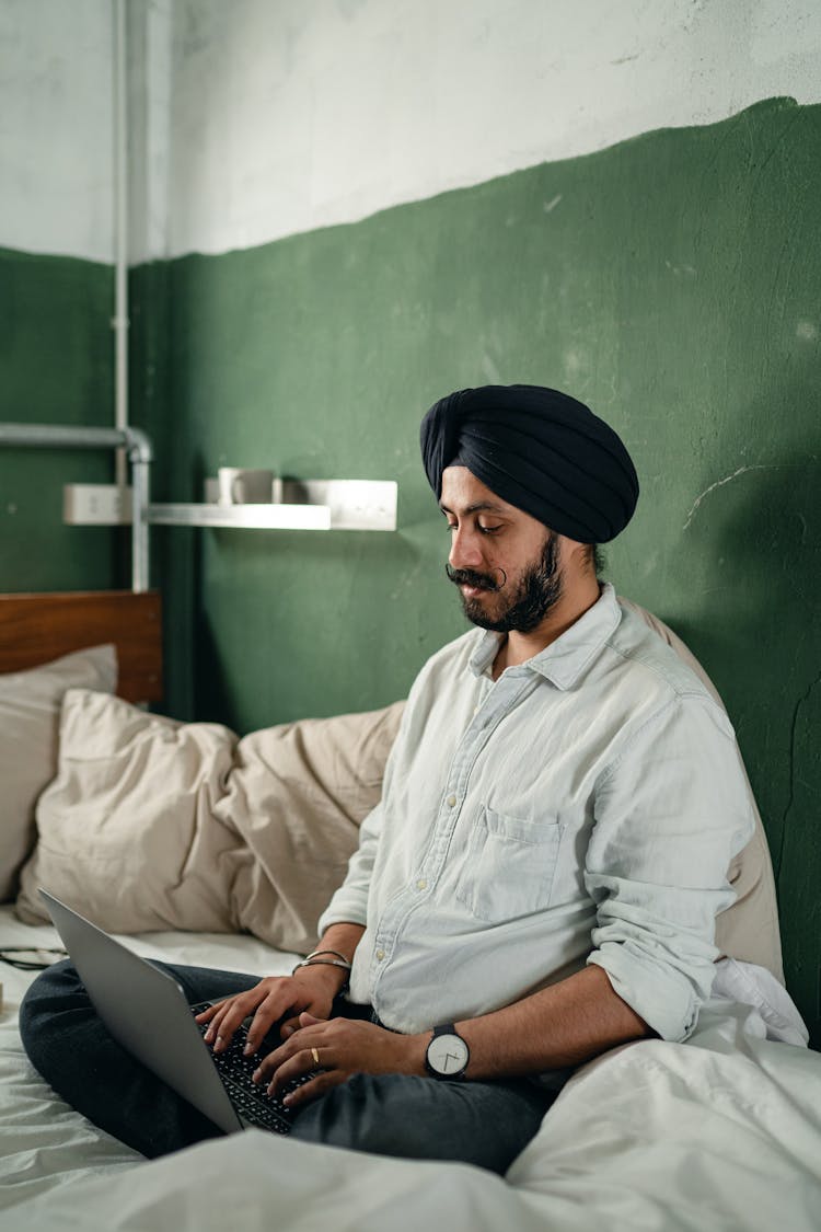 Serious Man Typing On Laptop In Bedroom