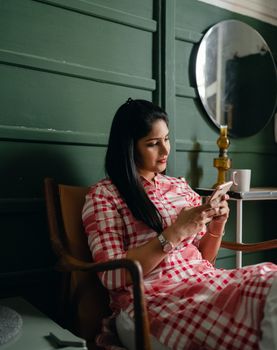 一位年轻女子穿着格子裙，在室内放松地玩着手机，营造出舒适的氛围