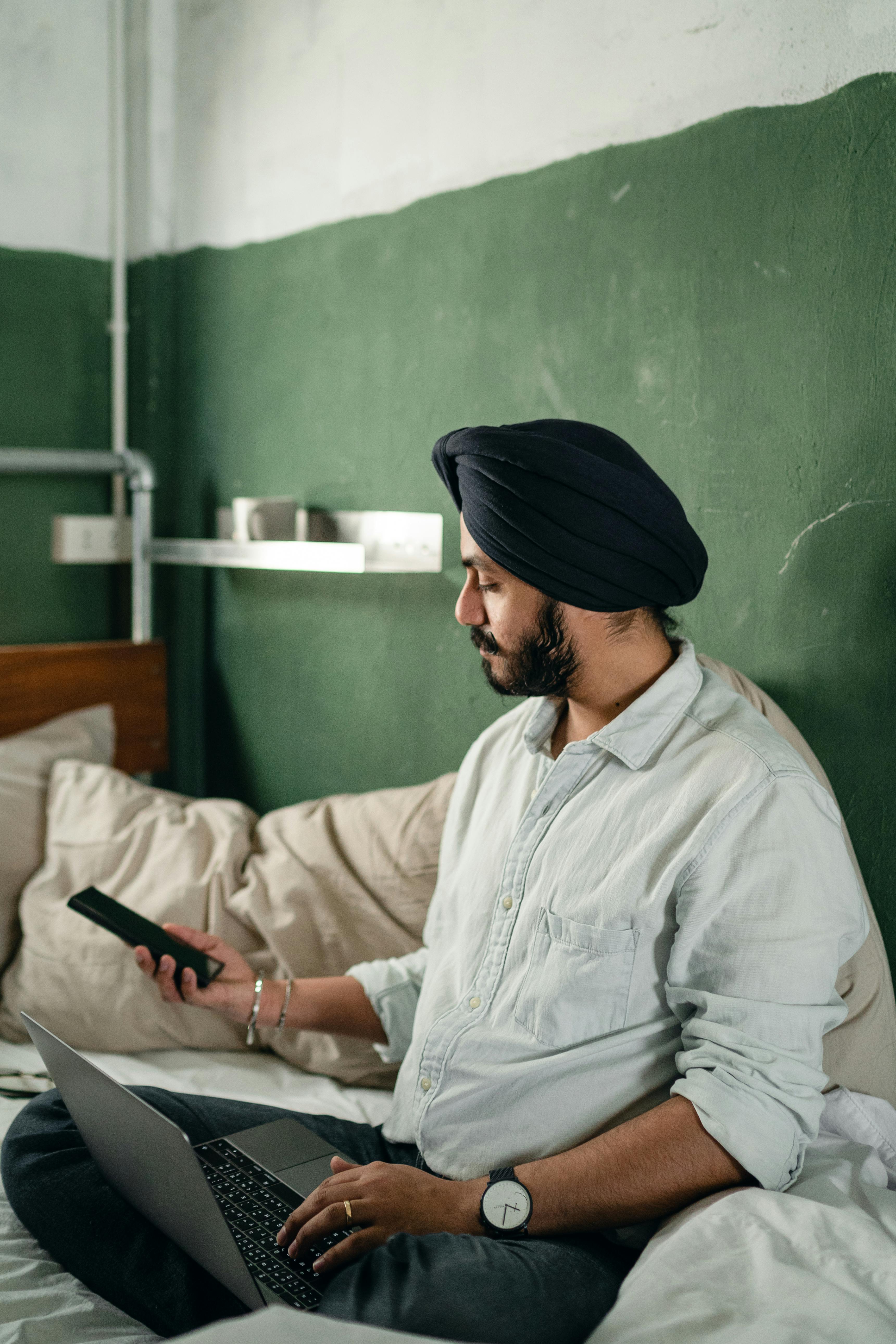 Calm busy man in turban using smartphone and laptop