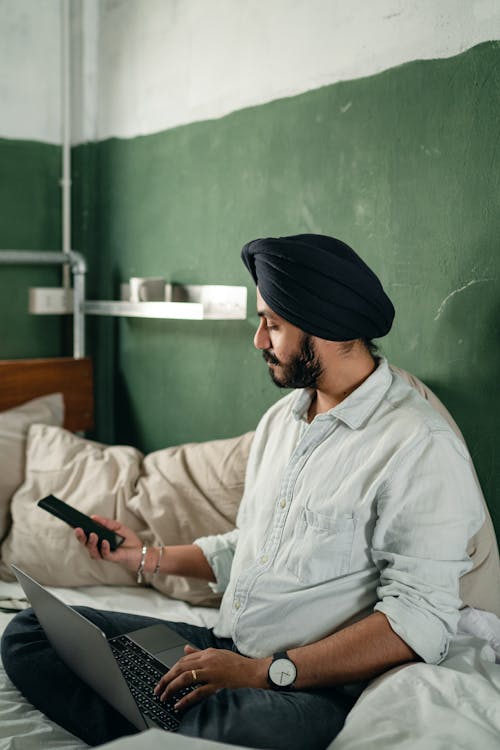Free Calm busy man in turban using smartphone and laptop Stock Photo