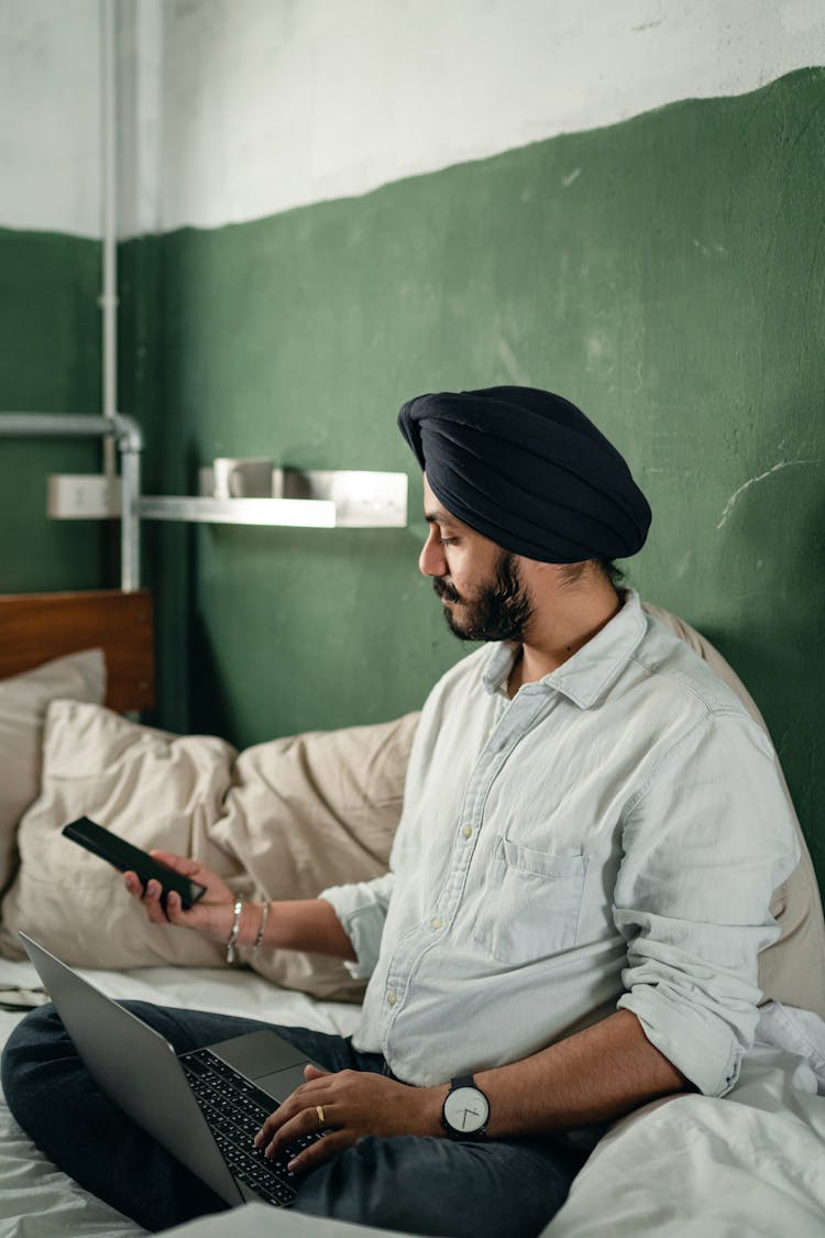 Calm Busy Man In Turban Using Smartphone And Laptop