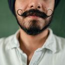 Crop anonymous adult ethnic male with black beard and thick mustache curled upward in casual wear against green background