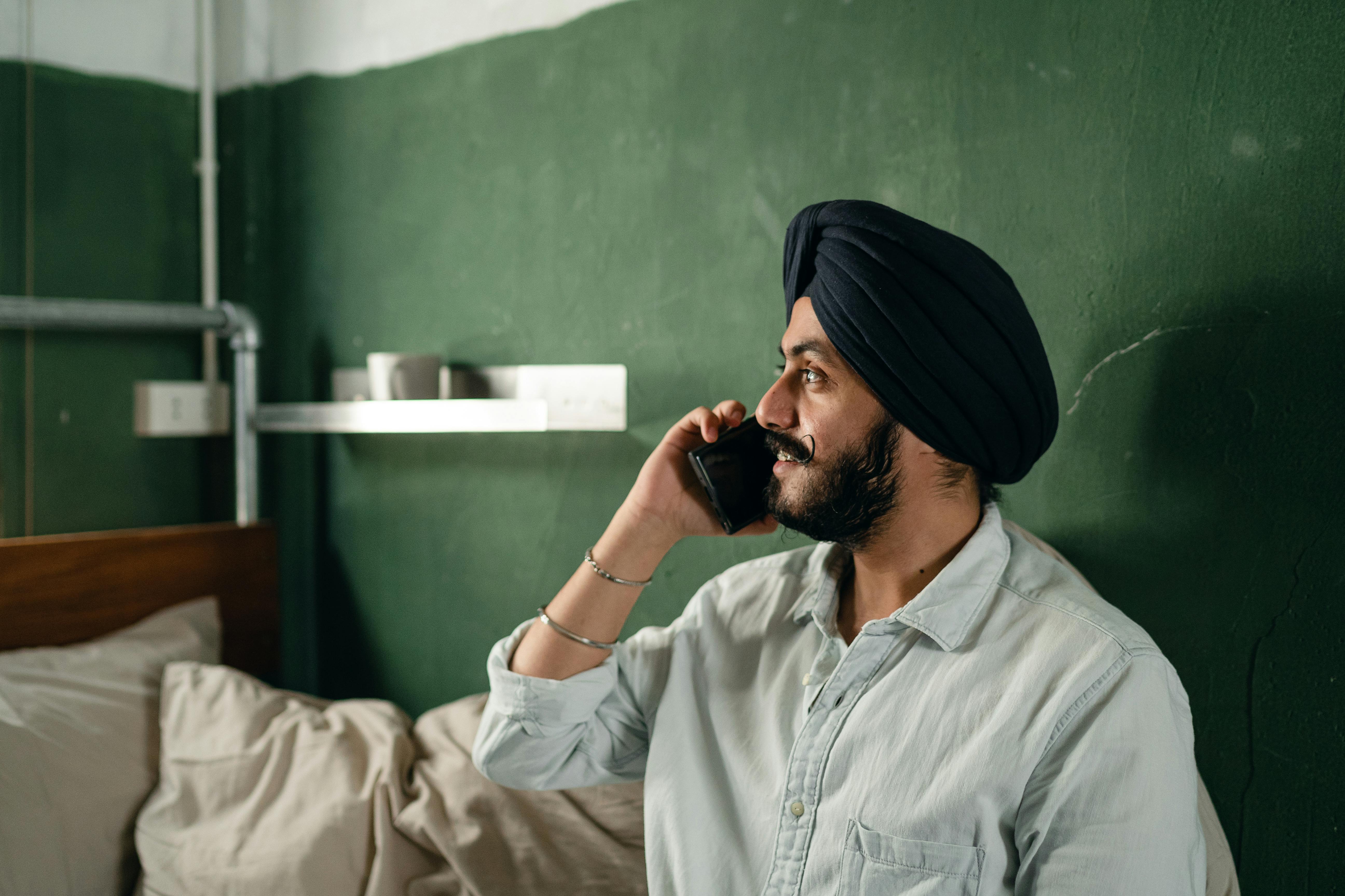 bearded indian man communicating on smartphone in plainly furnished room