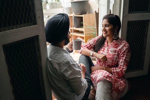 Free Young Indian spouses having pleasant conversation and drinking coffee while sitting on floor at home on day off Stock Photo