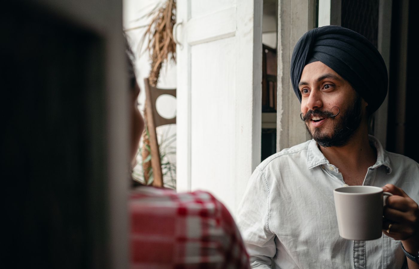 A cheerful man with a turban enjoying coffee and conversation indoors.