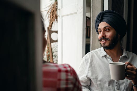 A cheerful man with a turban enjoying coffee and conversation indoors.