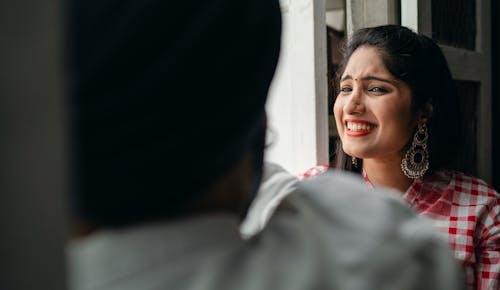 Elegant young Indian lady in checkered shirt laughing tears at hilarious story told by anonymous blurred male