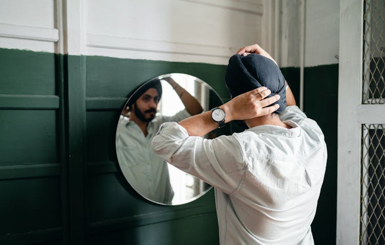 Young Indian Man Adjusting Turban Against Mirror