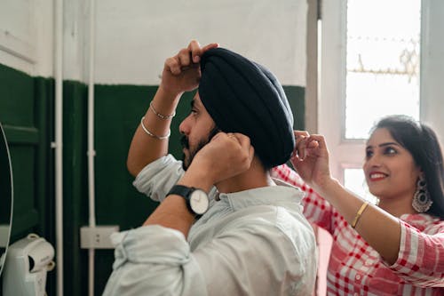 Loving young wife helping bearded husband with traditional turban