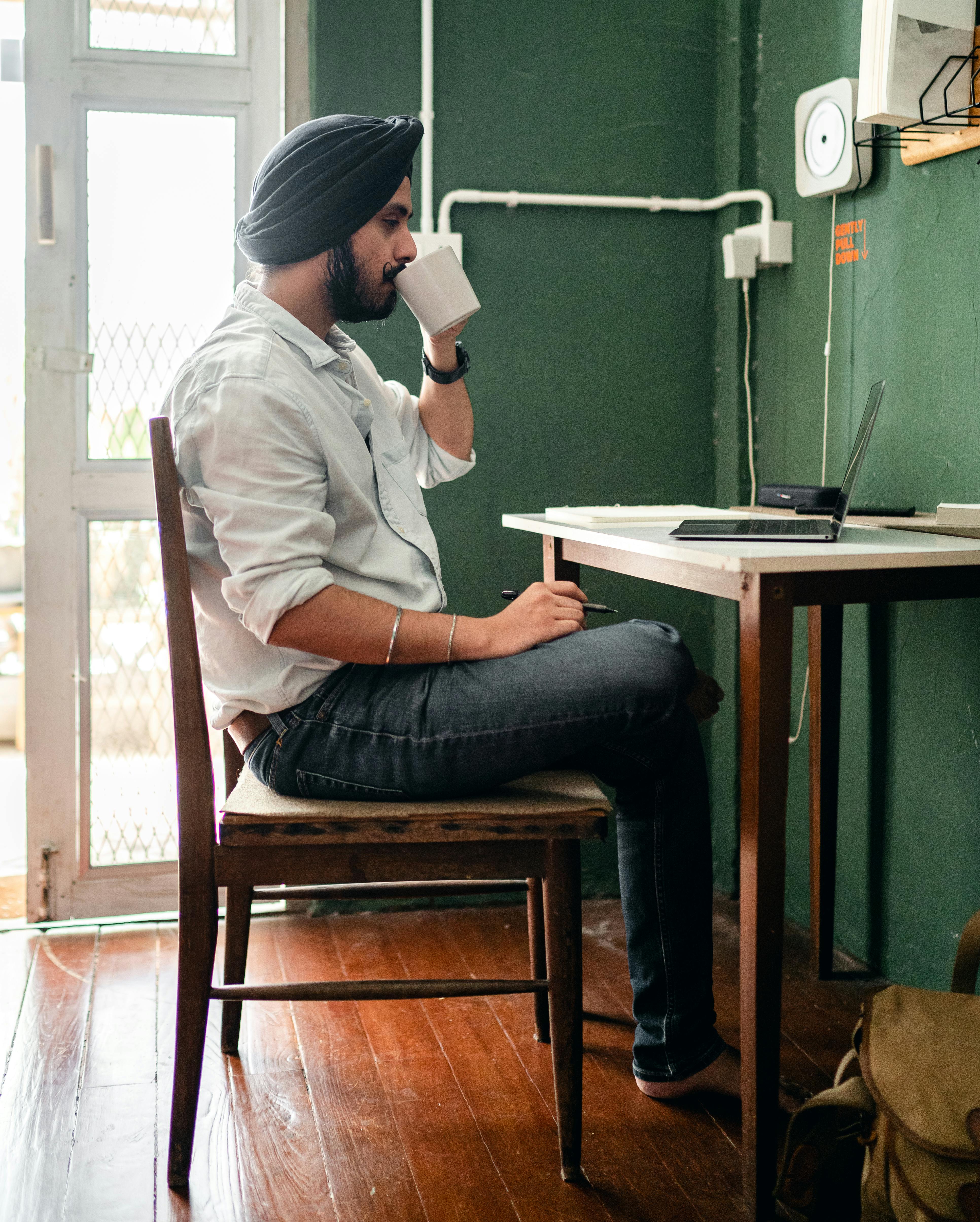 Young Indian man sitting at table with netbook and drinking coffee