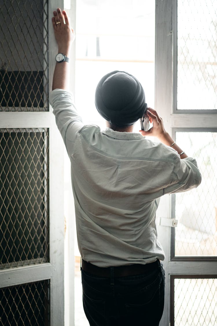 Faceless Young Sikh Man Talking On Smartphone Standing Near Window