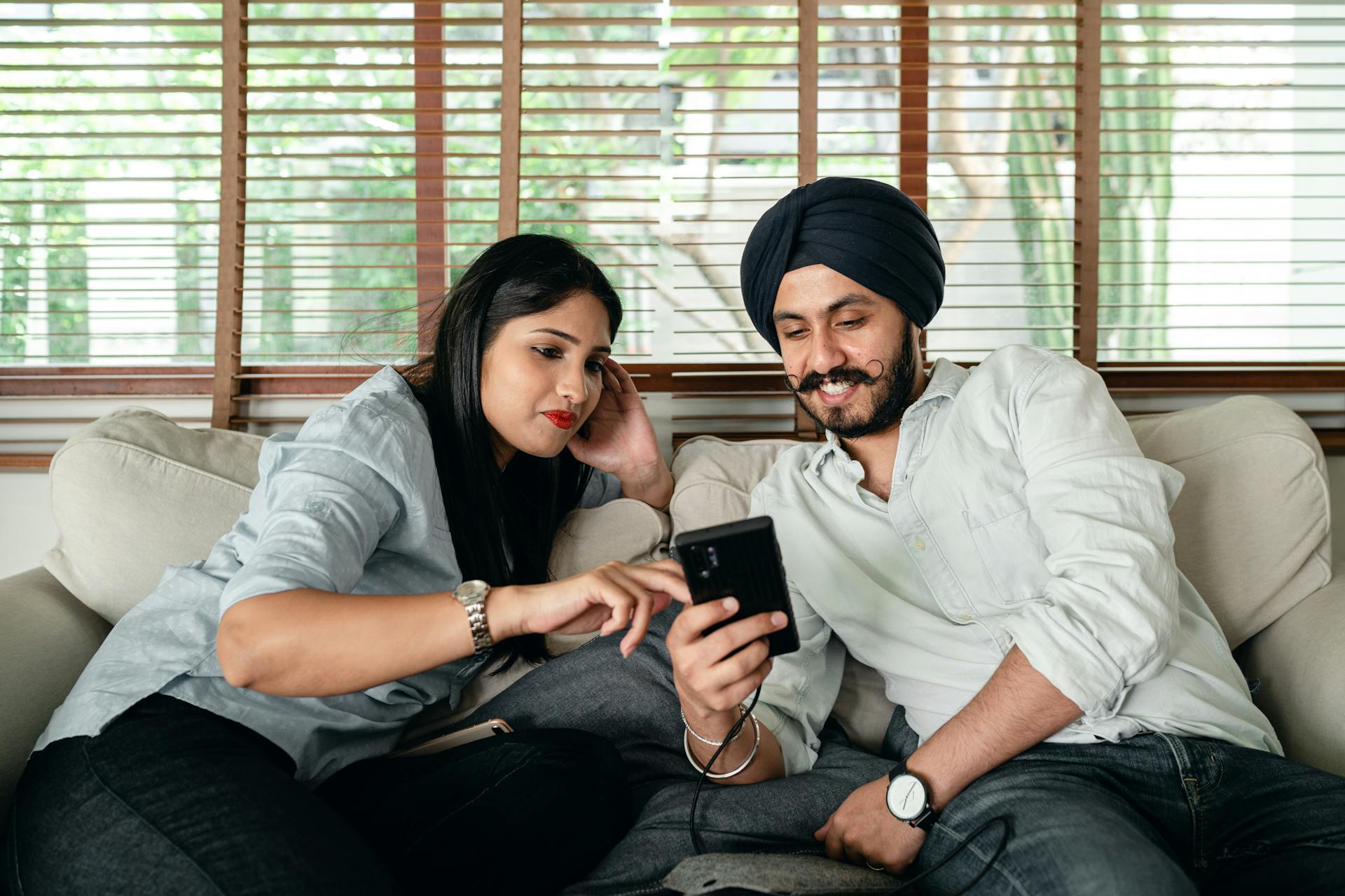 A young couple enjoying quality time at home, sharing moments on a smartphone while relaxing on the couch.