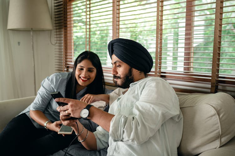 Young Indian Couple Watching Video On Smartphone Sitting On Couch