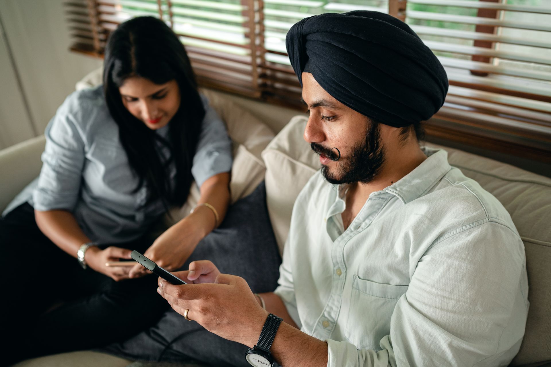 A young couple relaxing on a sofa, browsing on their smartphones in a cozy indoor setting.