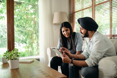 Free Young Indian man in casual outfit and turban working on project with female colleague using tablet in cozy workplace Stock Photo