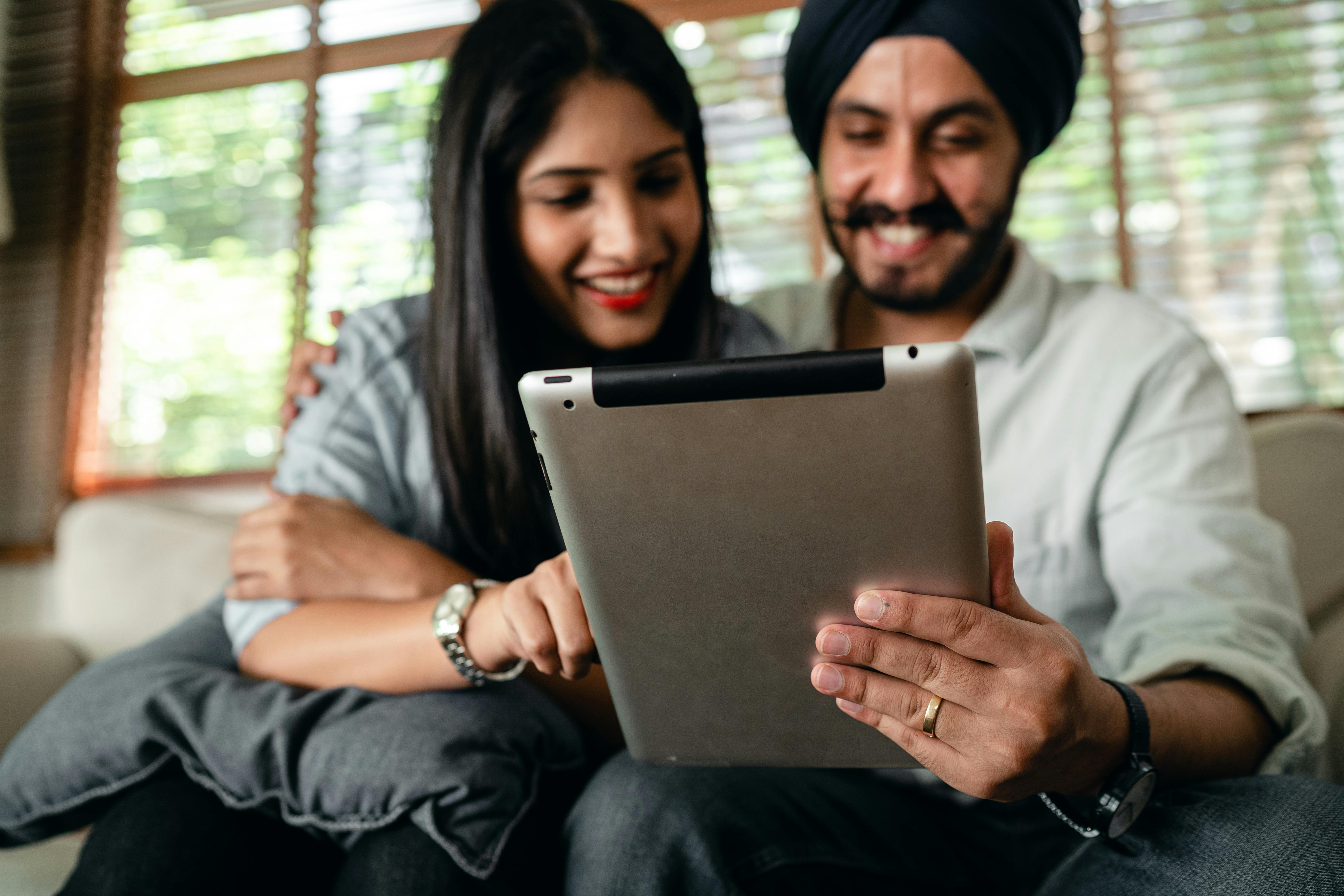 joyful young indian couple watching video on tablet and having fun