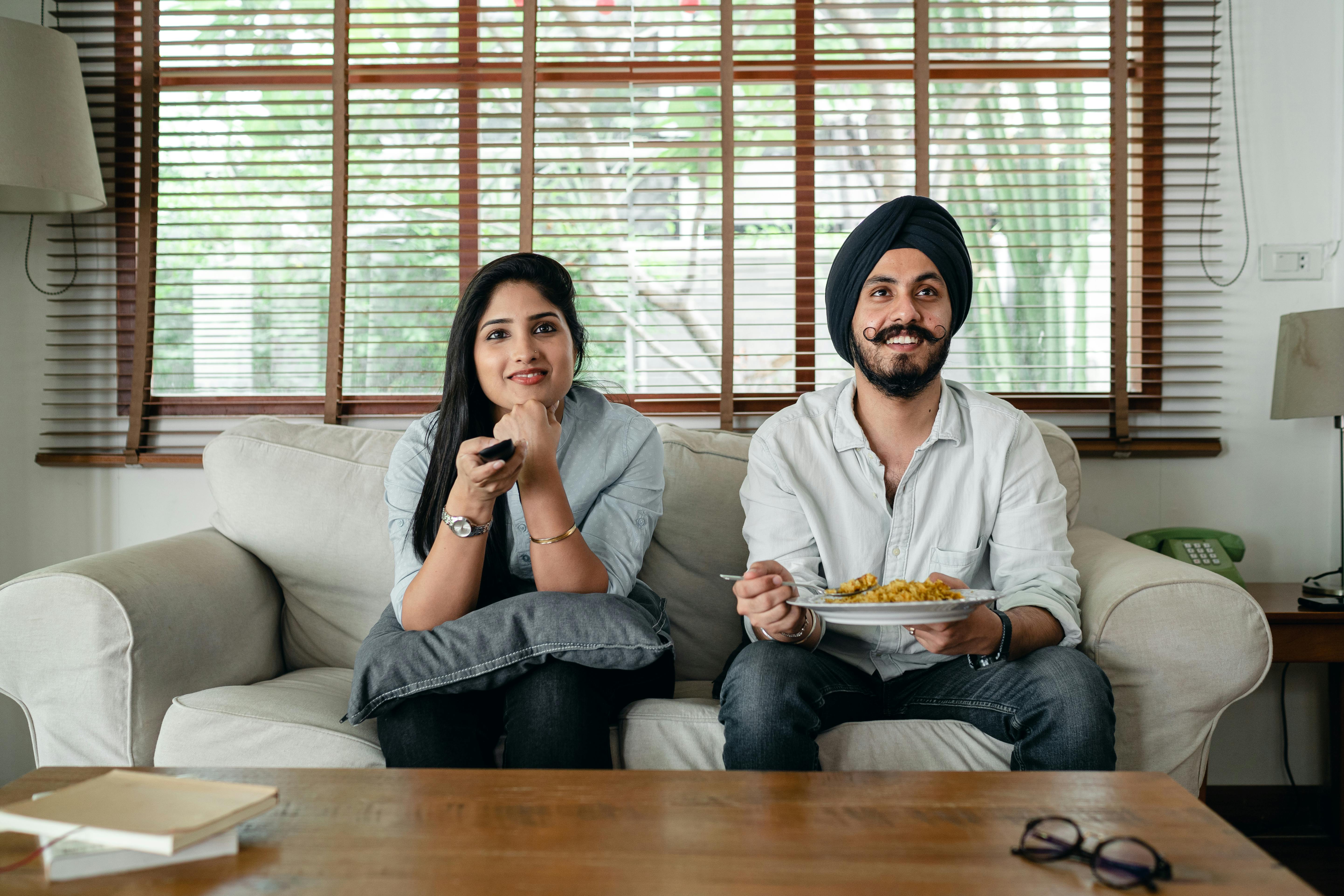 smiling ethnic couple sitting on sofa and watching movie