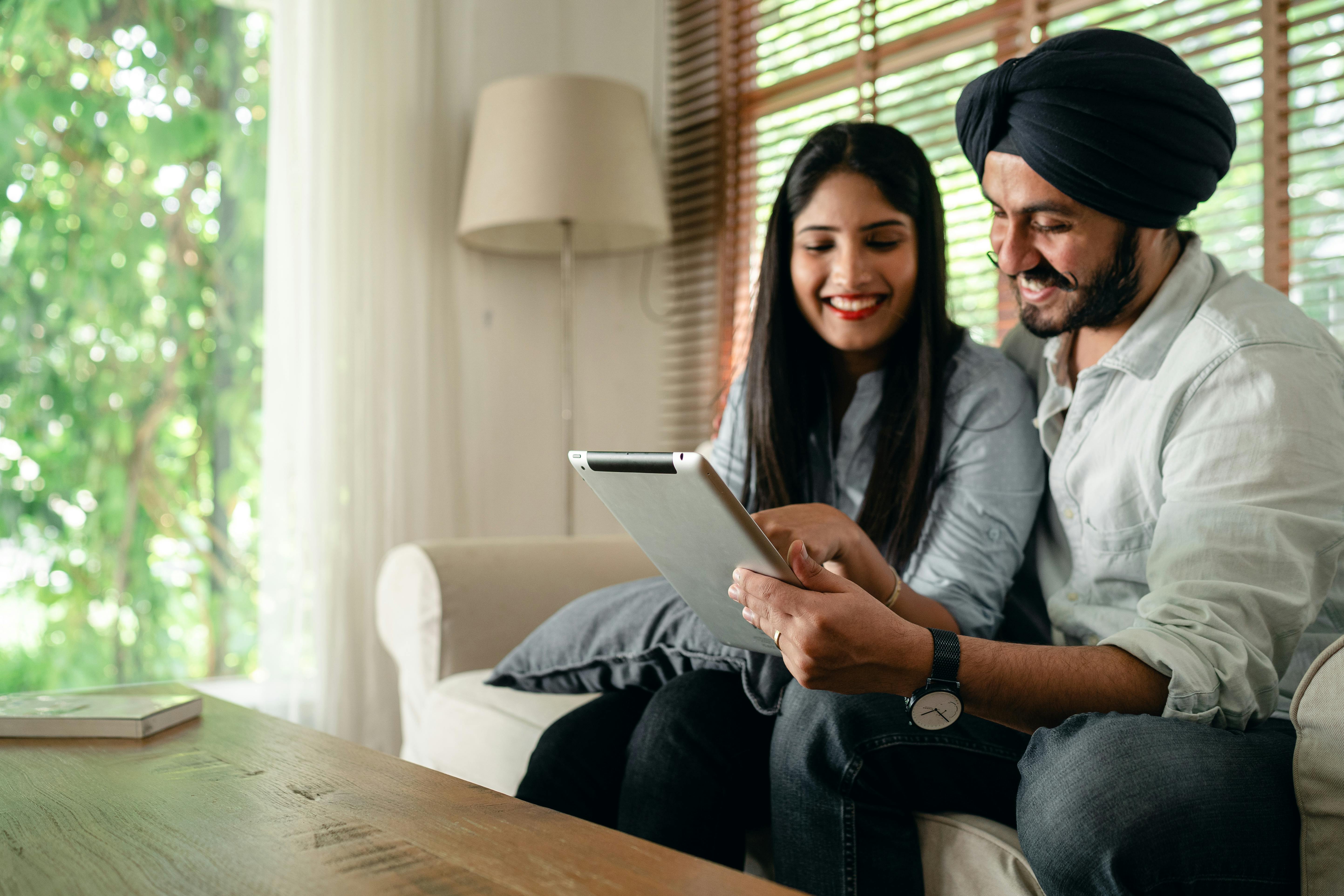 positive indian couple using tablet in living room