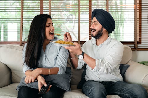 Delighted ethnic couple having meal on sofa in living room