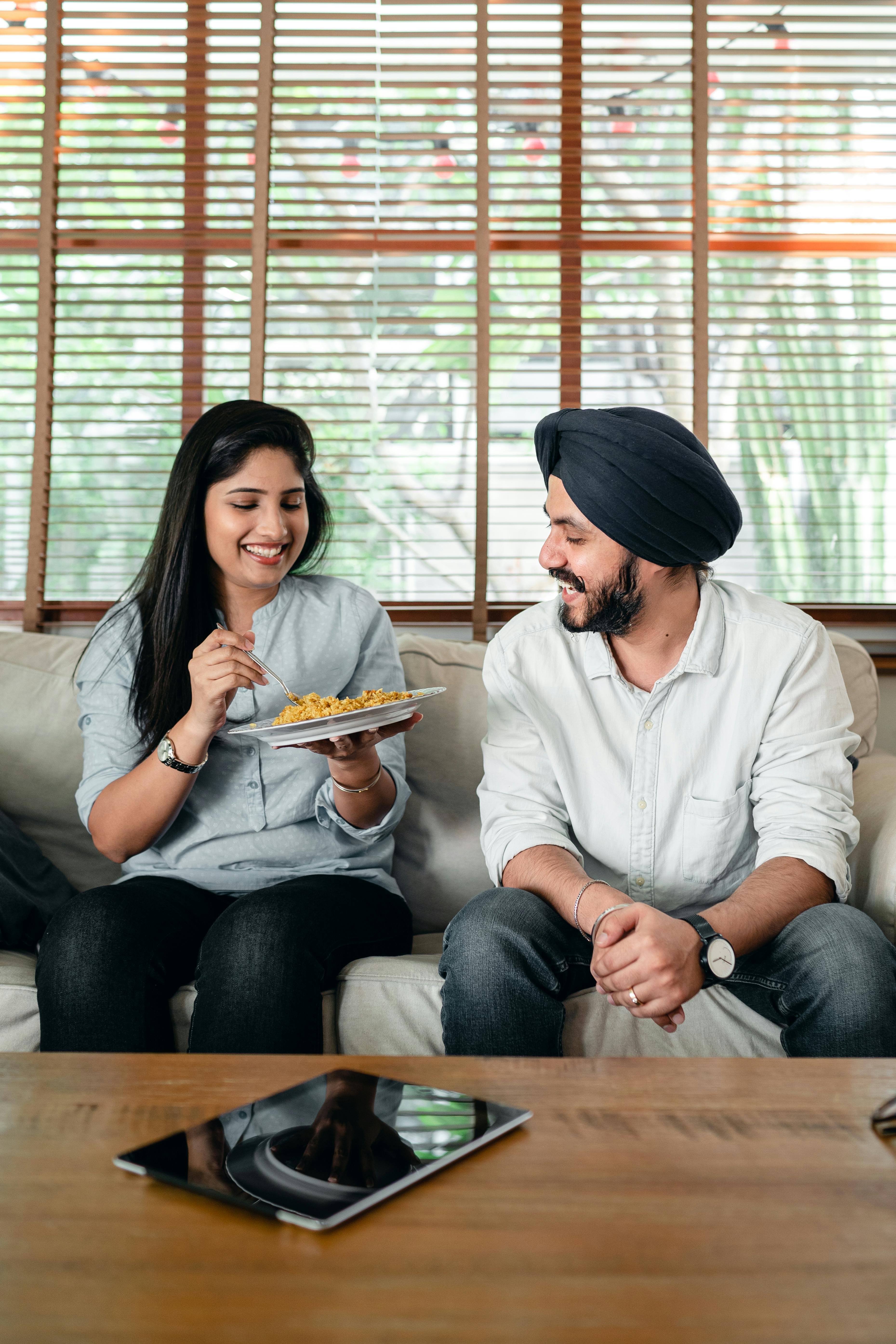 cheerful young indian couple having lunch together on couch