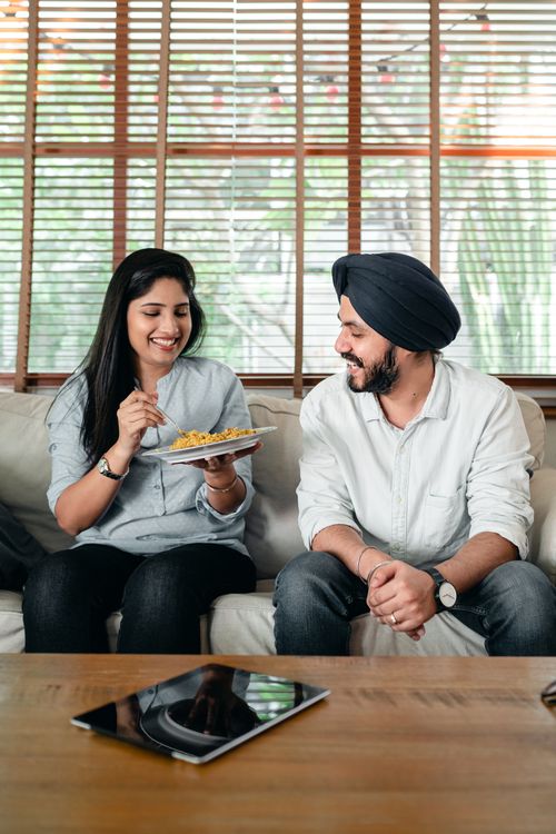 Free Happy young Indian woman and man in casual wear relaxing on sofa at home and eating plate of delicious saffron rice Stock Photo
