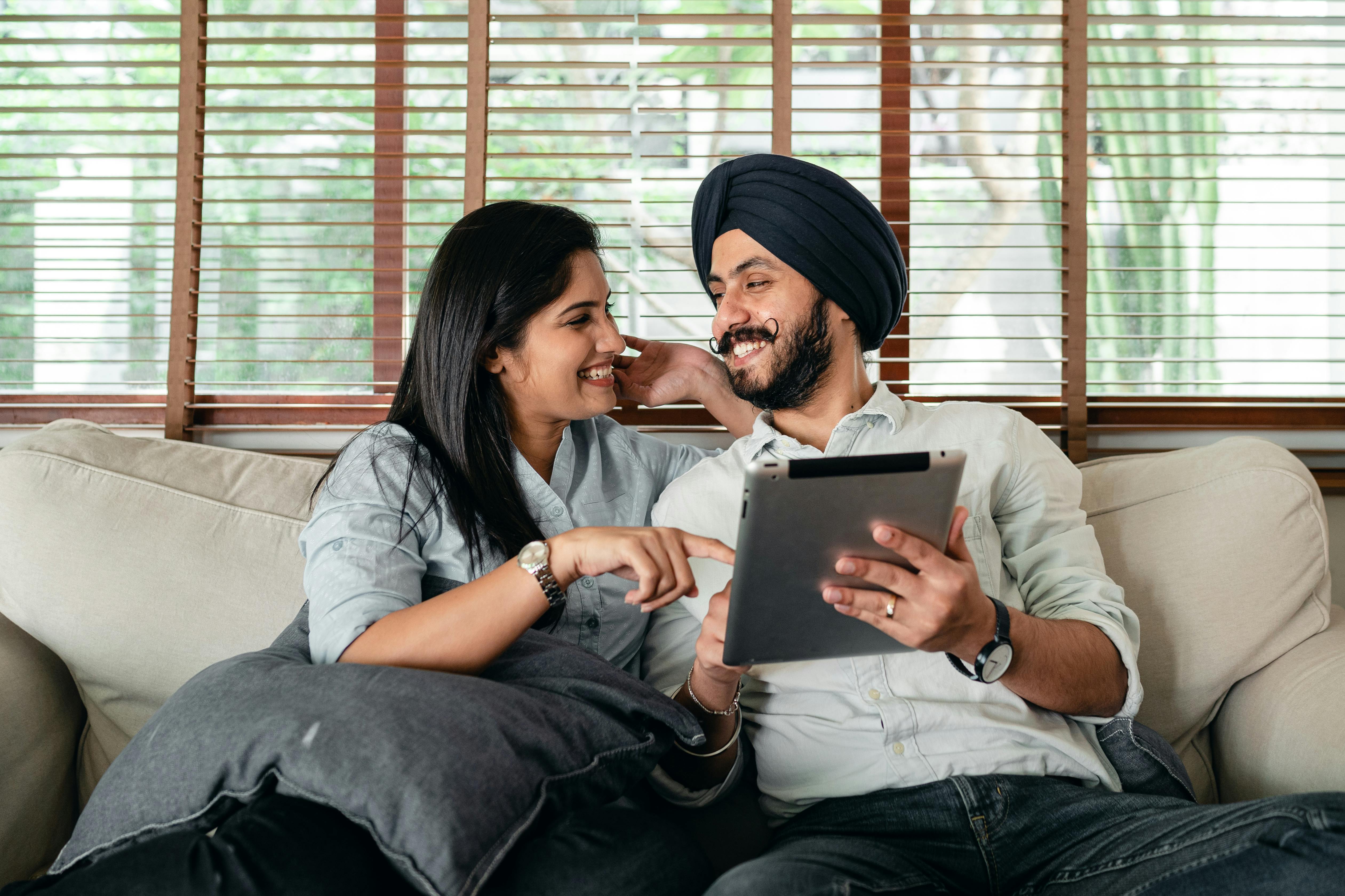 smiling young indian couple watching movie on tablet sitting on soft couch