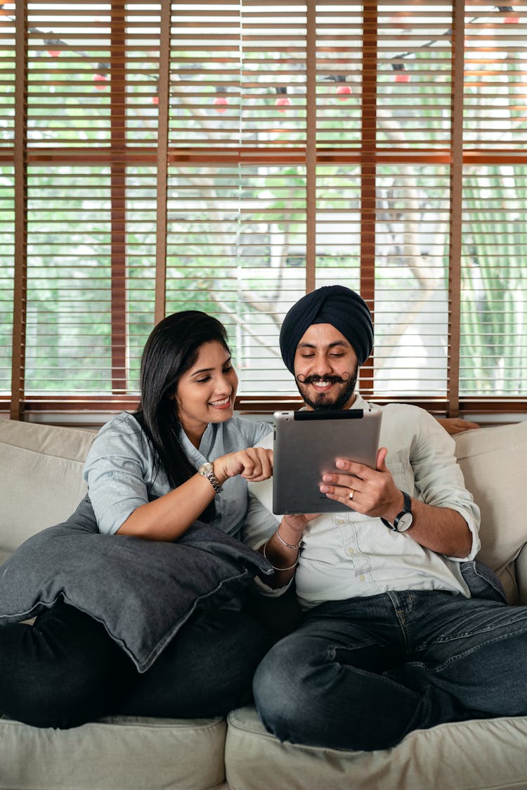 Happy Indian Couple Spending Weekend Together On Couch With Tablet