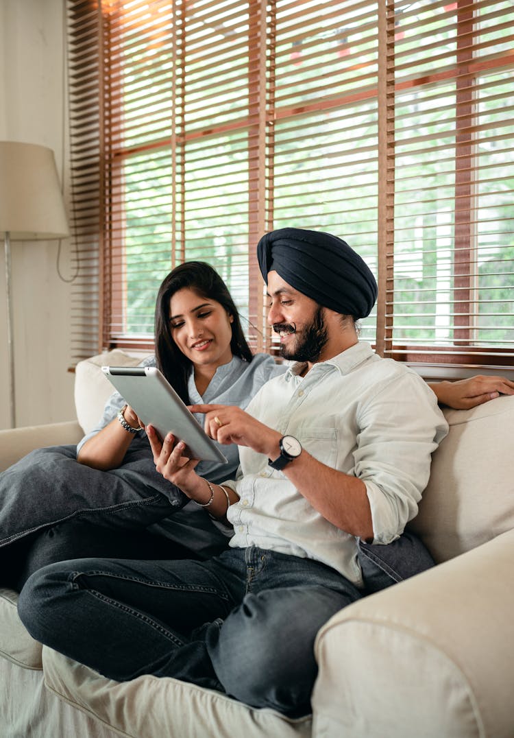 Optimistic Young Indian Couple Browsing Tablet On Couch