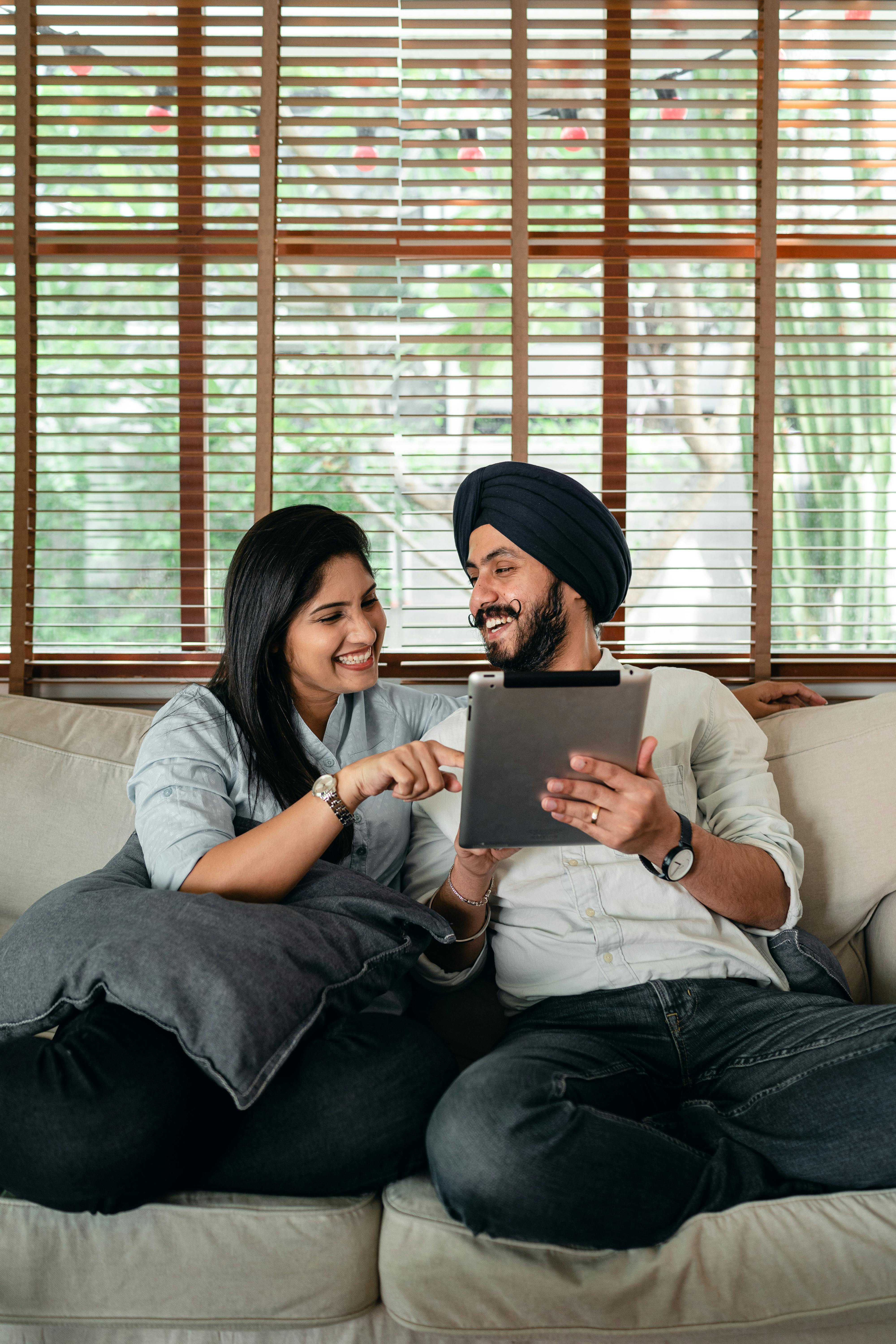 joyful young indian couple having fun while browsing tablet on couch