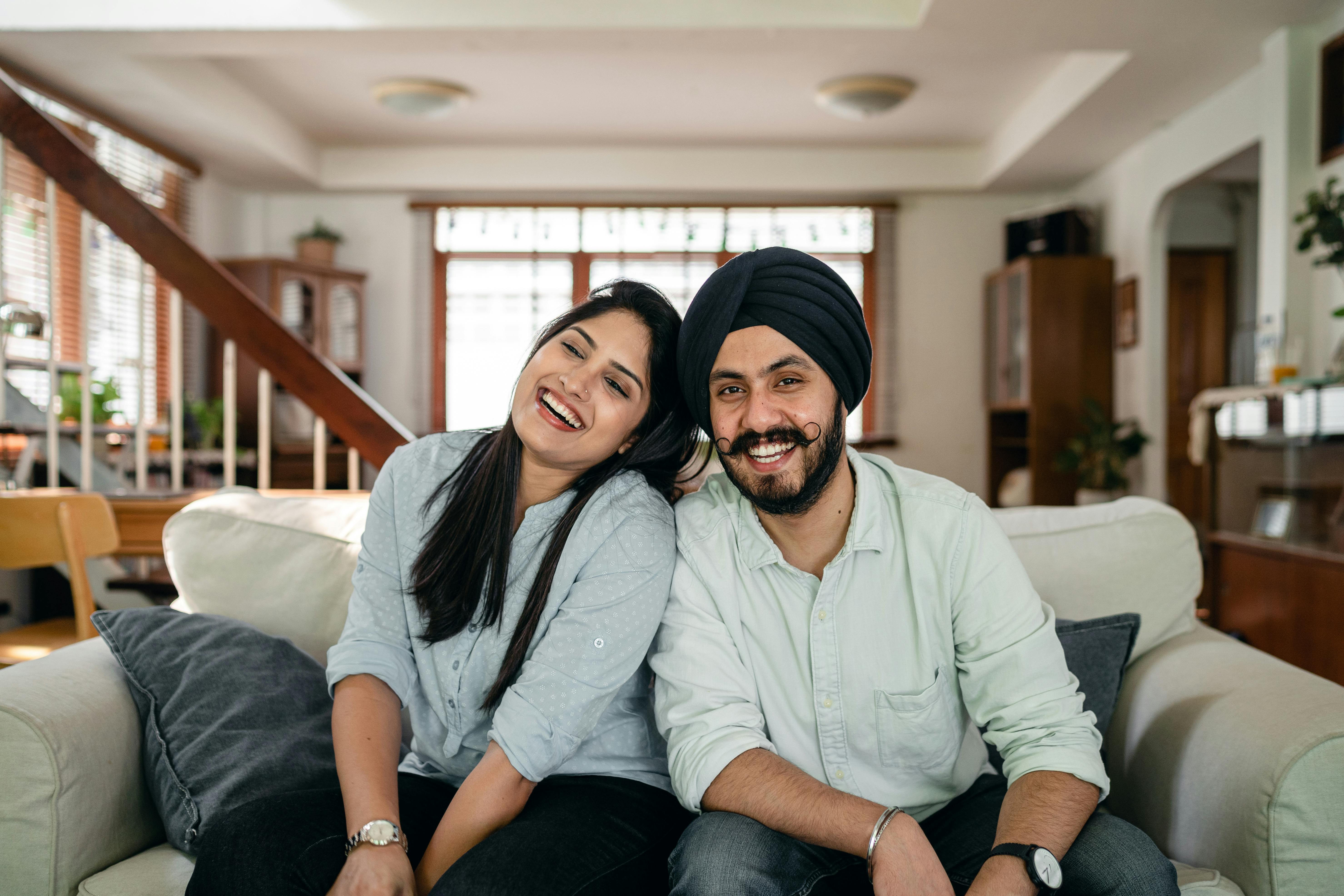 delighted young indian couple relaxing and laughing together on couch at home