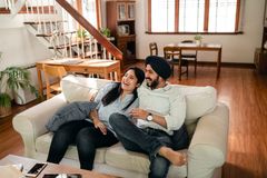 From above of joyful cuddling young Indian couple joking and laughing while resting together on comfortable sofa