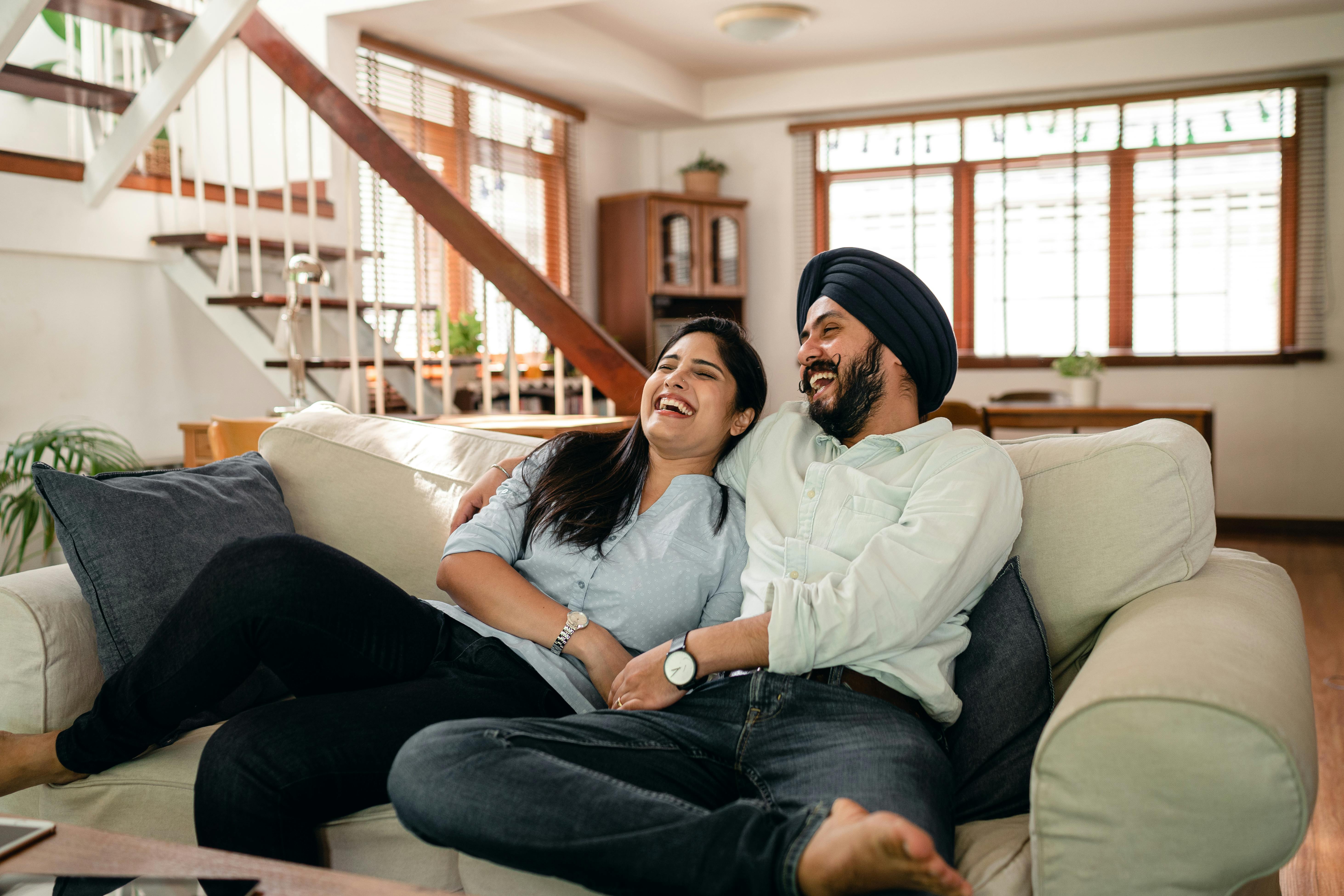 laughing young indian couple watching comedy movie together at home