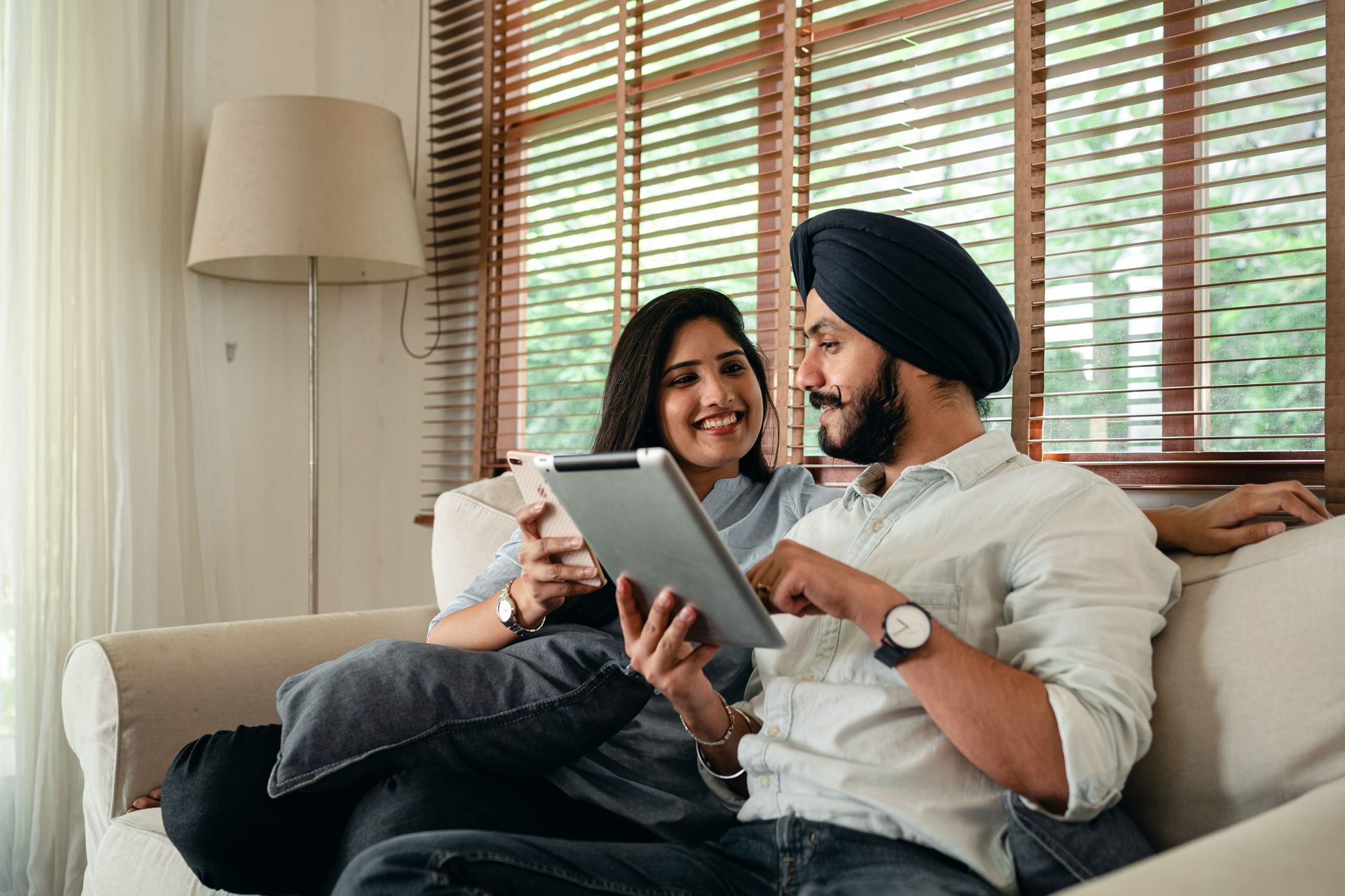 Indian couple with tablet and smartphone on couch at home