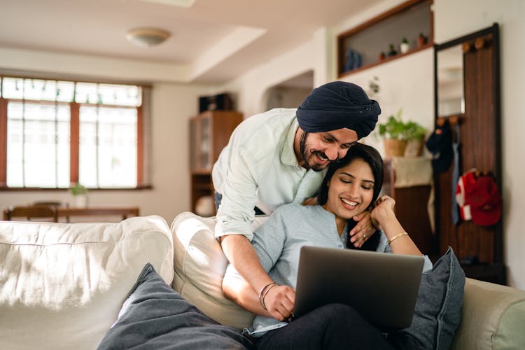 Happy Ethnic Couple Browsing Laptop In Modern Apartment