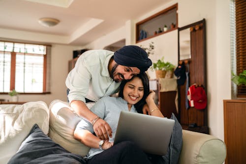 Cheerful ethnic couple surfing laptop together at home