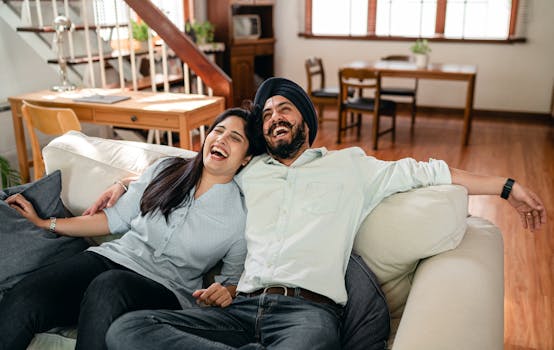 A joyful couple laughing and relaxing together on a cozy sofa in a brightly lit living room.