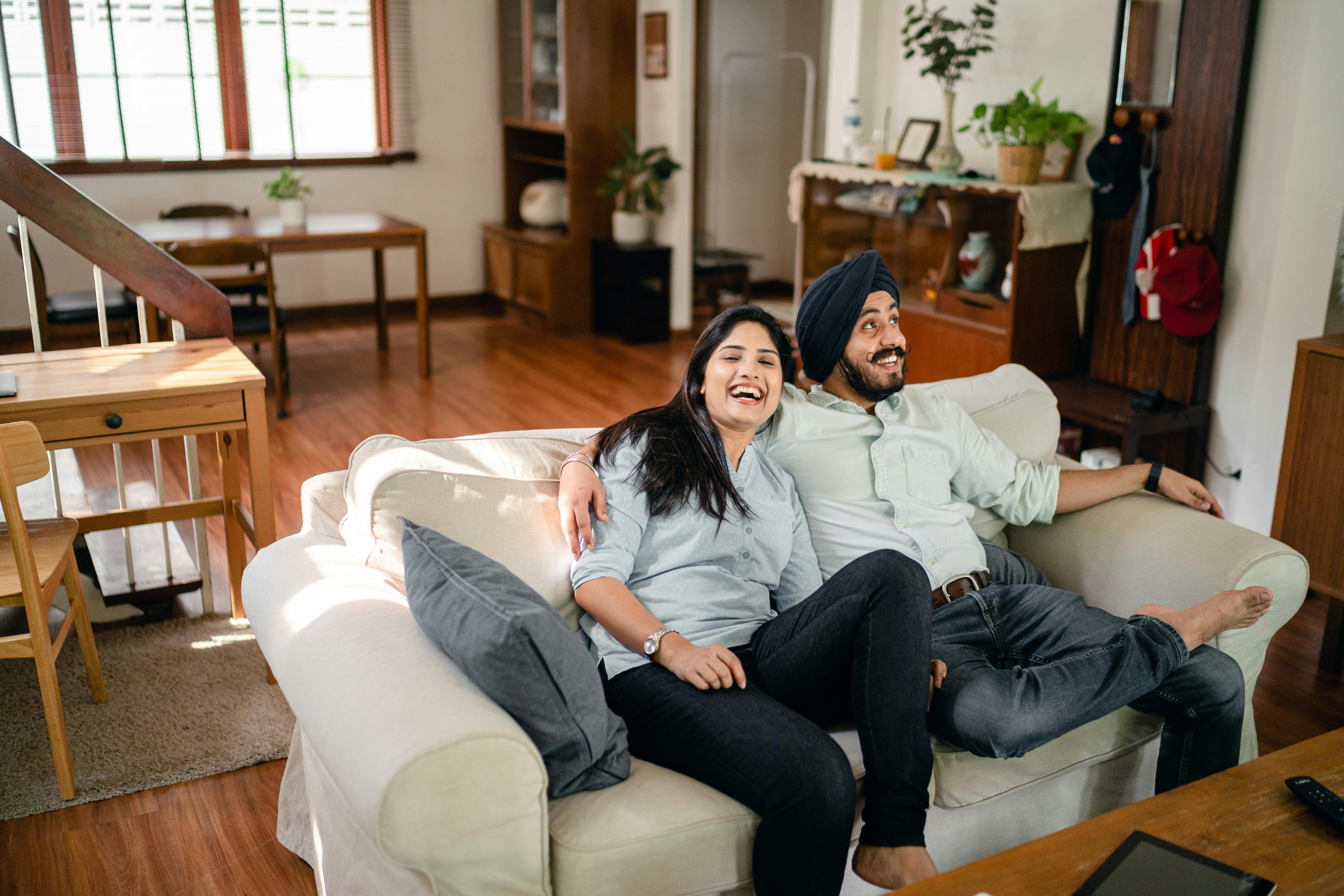 delighted indian couple hugging on sofa in cozy apartment