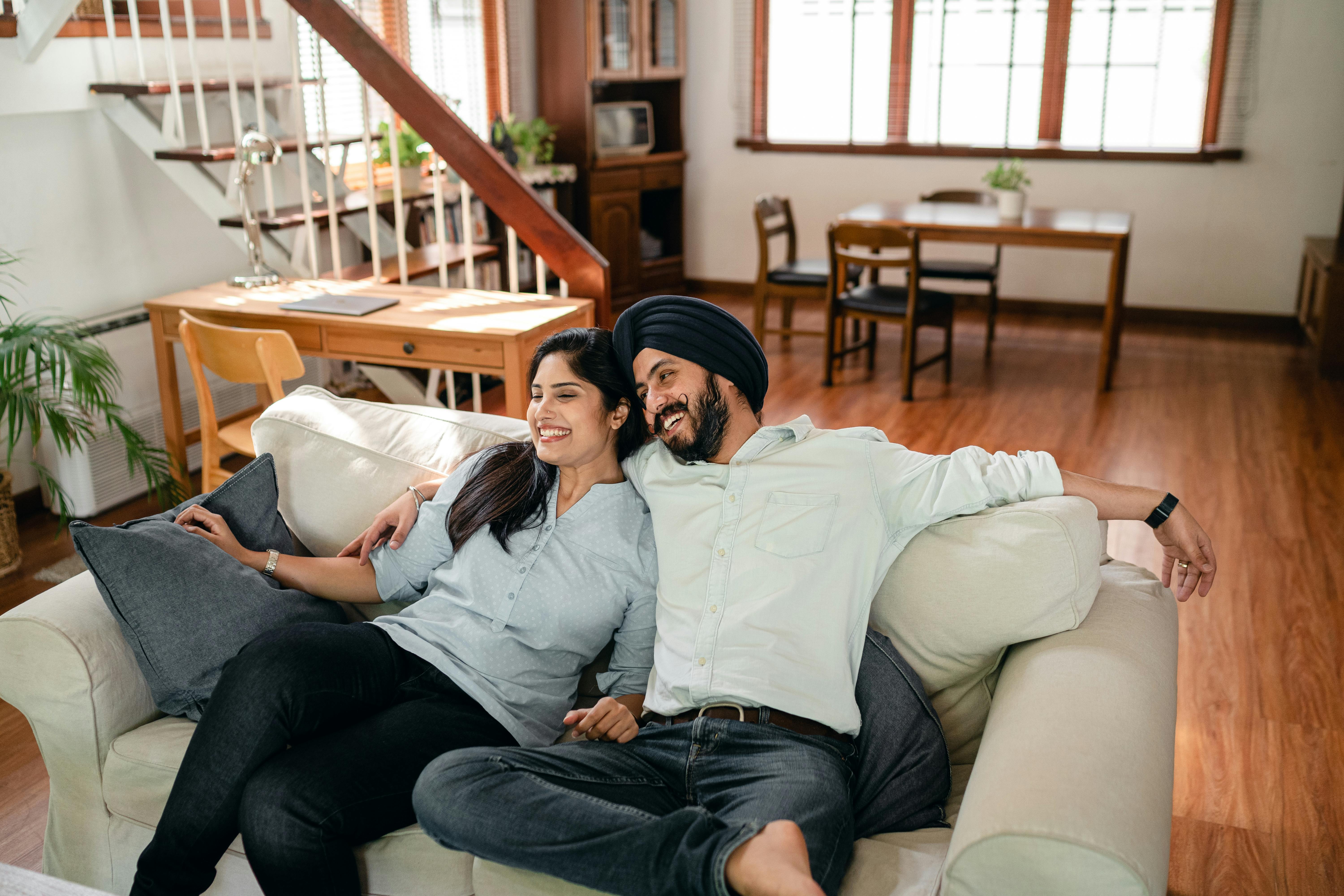 From above of optimistic ethnic man and woman in casual outfit embracing and resting together on cozy sofa while enjoying romantic holiday at home