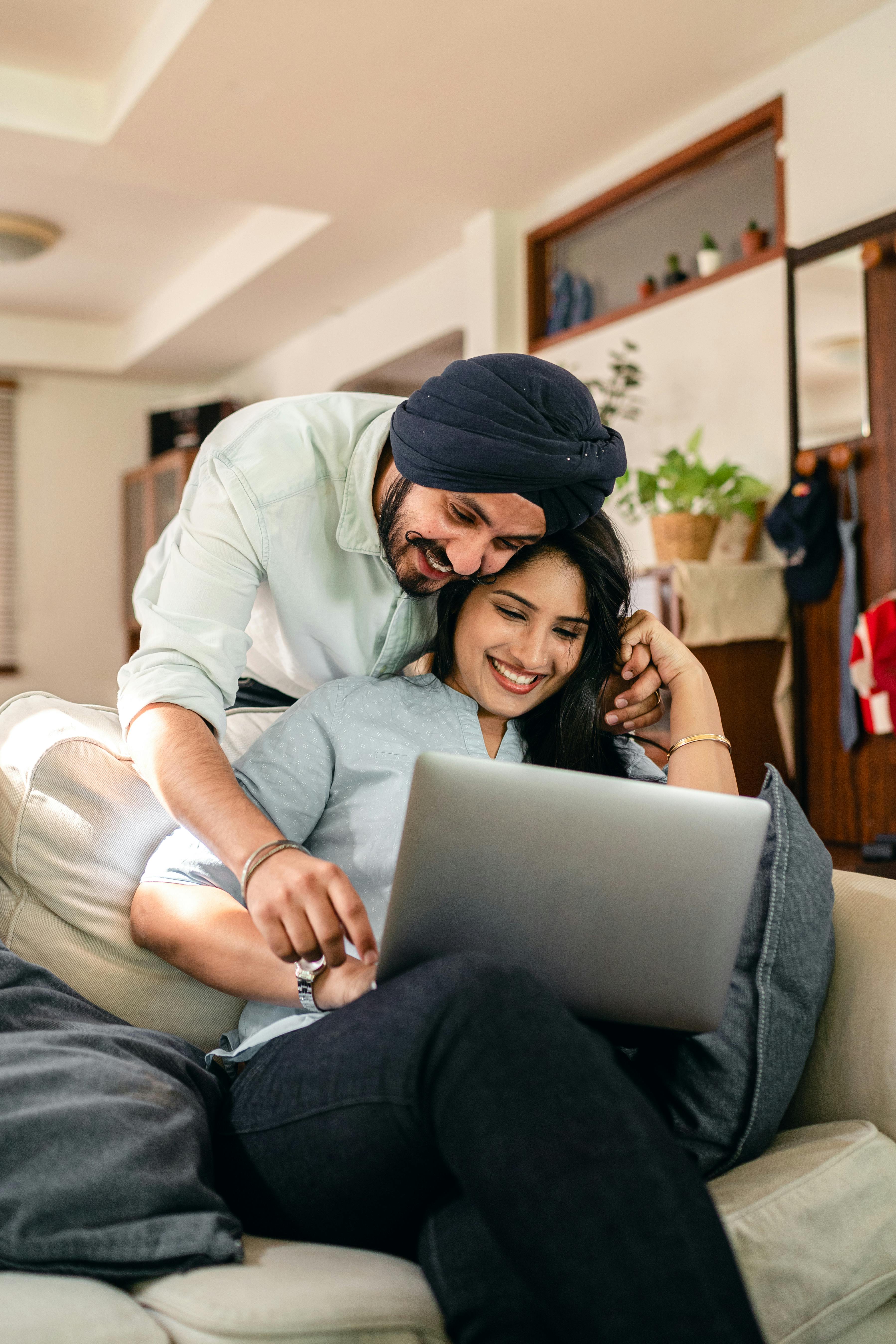 happy ethnic couple using laptop in living room together