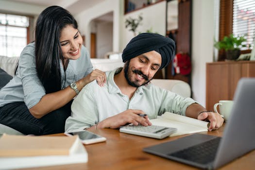 A smiling couple collaborates on financial paperwork at home, using a laptop and calculator.