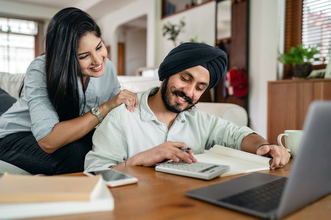 Smiling ethnic accountant using calculator while ethnic wife watching behind