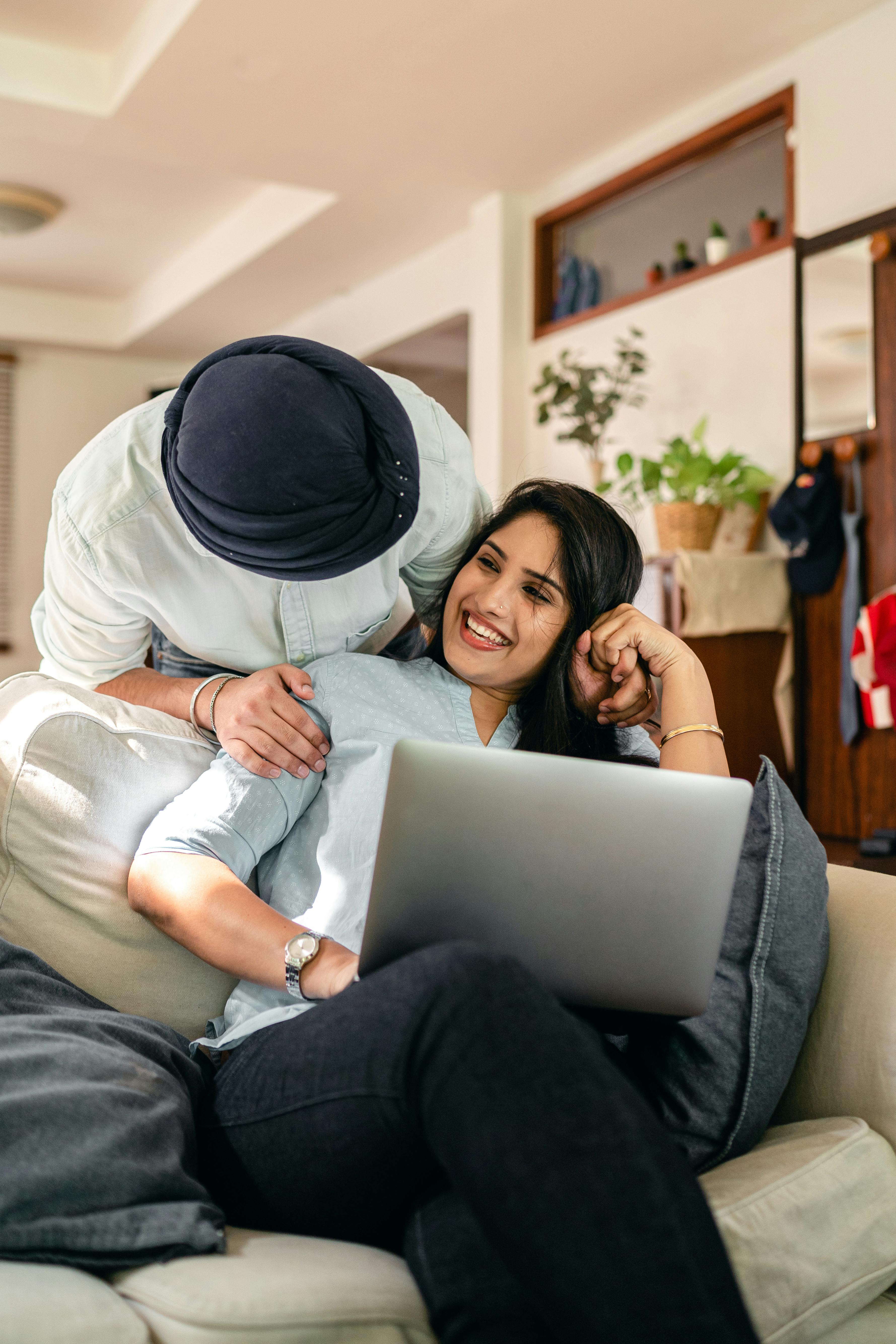 cheerful couple looking at each other while using laptop together