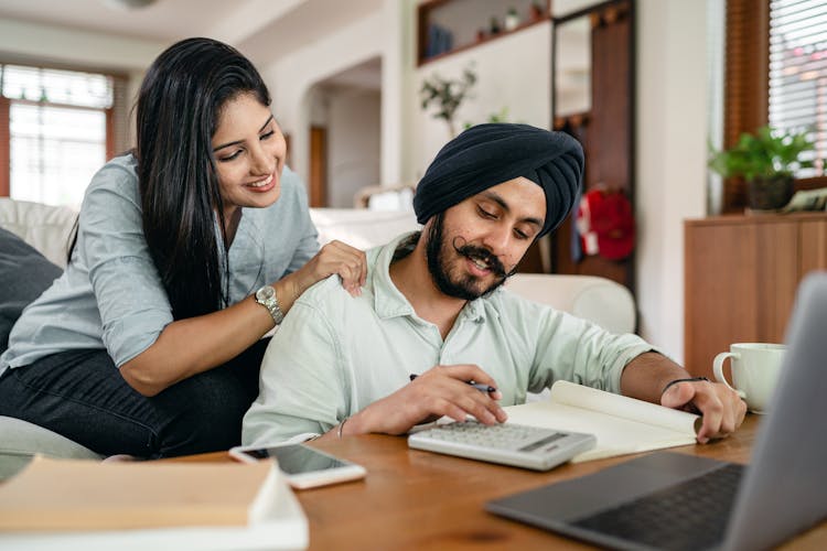 Happy Young Indian Woman Supporting Husband During Freelance Work At Home