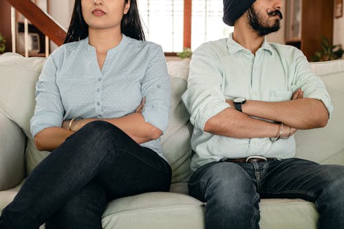 Free Crop faceless young ethnic couple in casual wear sitting on couch with arms crossed keeping silence after scandal at home Stock Photo